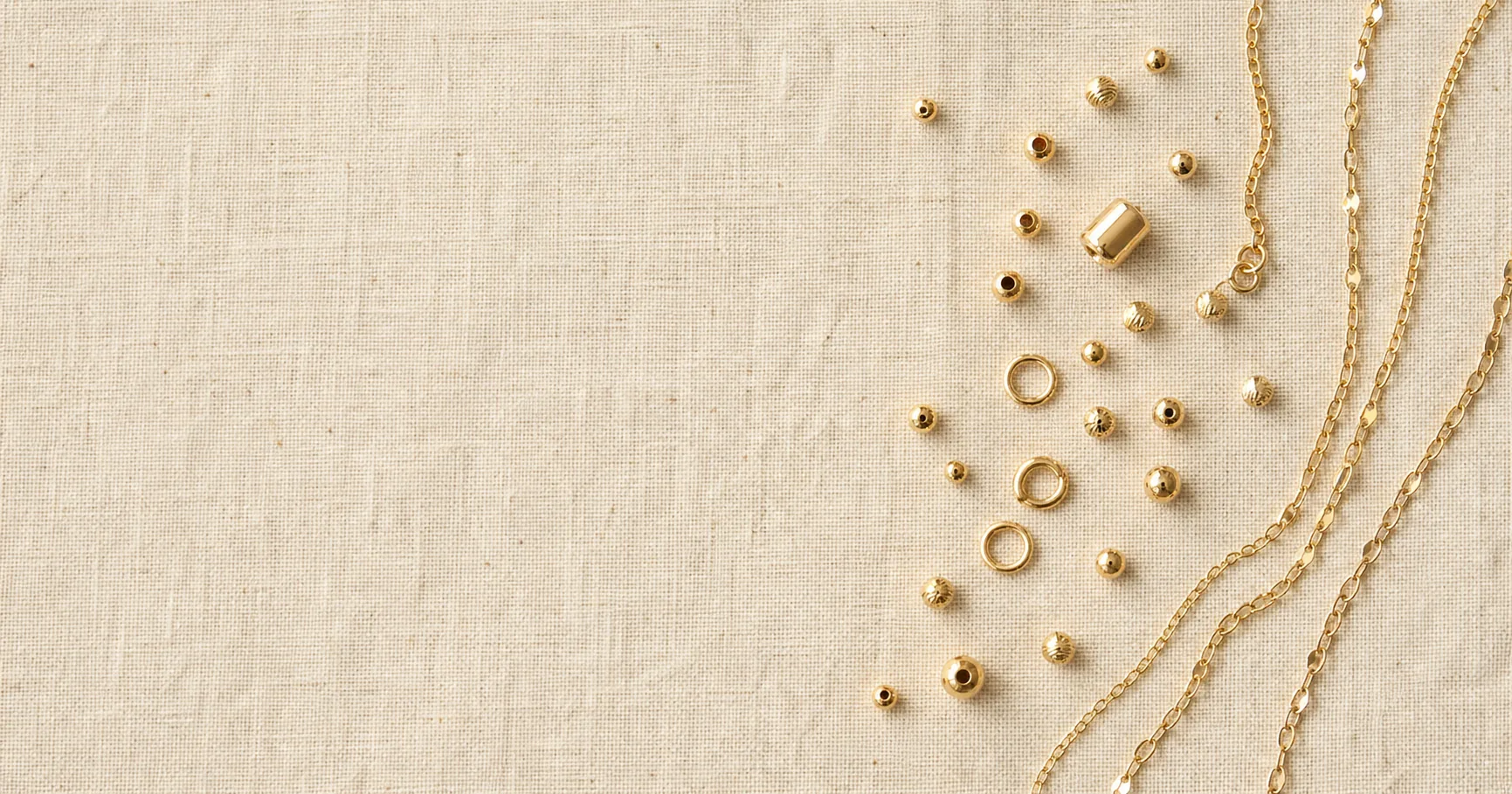 Flat-lay de bolas, argollas y cadenas en oro laminado 18k sobre lino natural